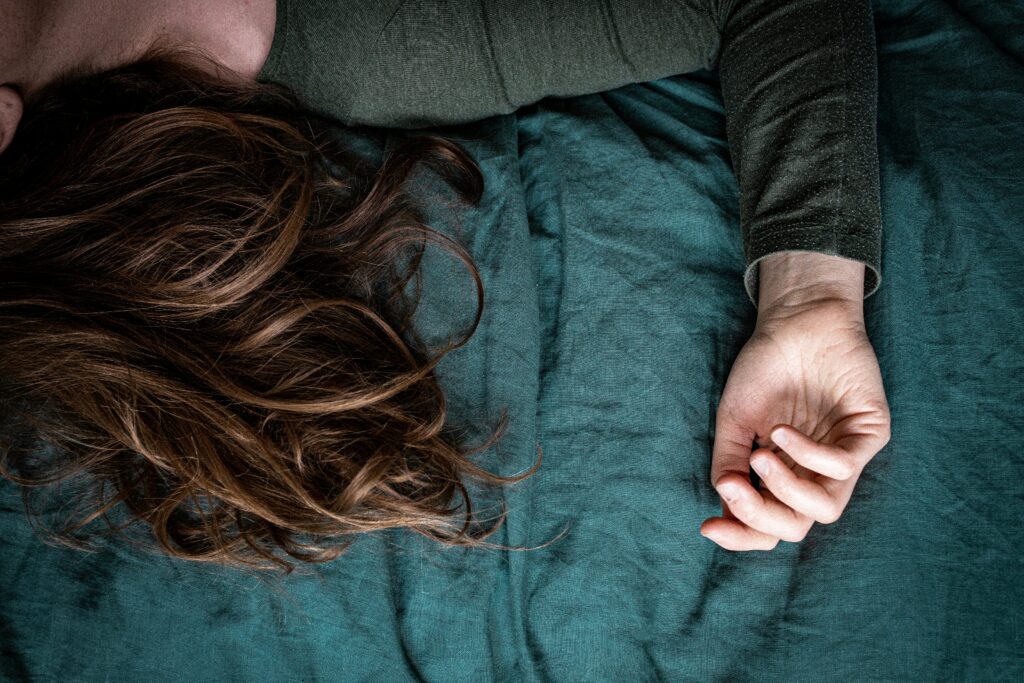 A cropped image seeing one arm and a partial part of someone's head laying down on teal sheets. The image alludes to the article that they may be sleeping alone due to their severe snoring.